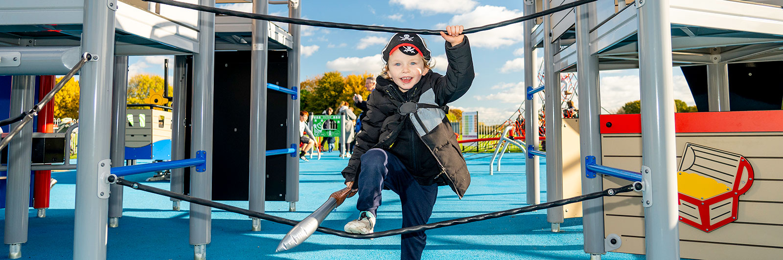 A young boy is dressed in fancy dress costume as a pirate and is playing at a pirate themed playground.